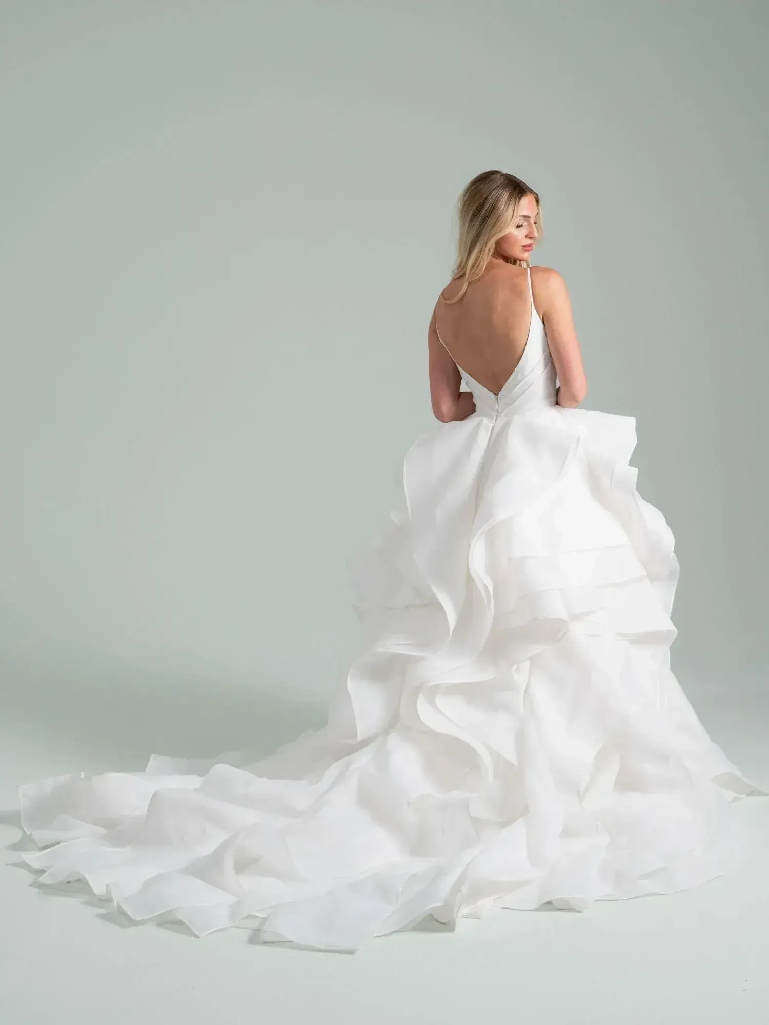 A woman in a flowing white dress with layered ruffles, seen from the back.