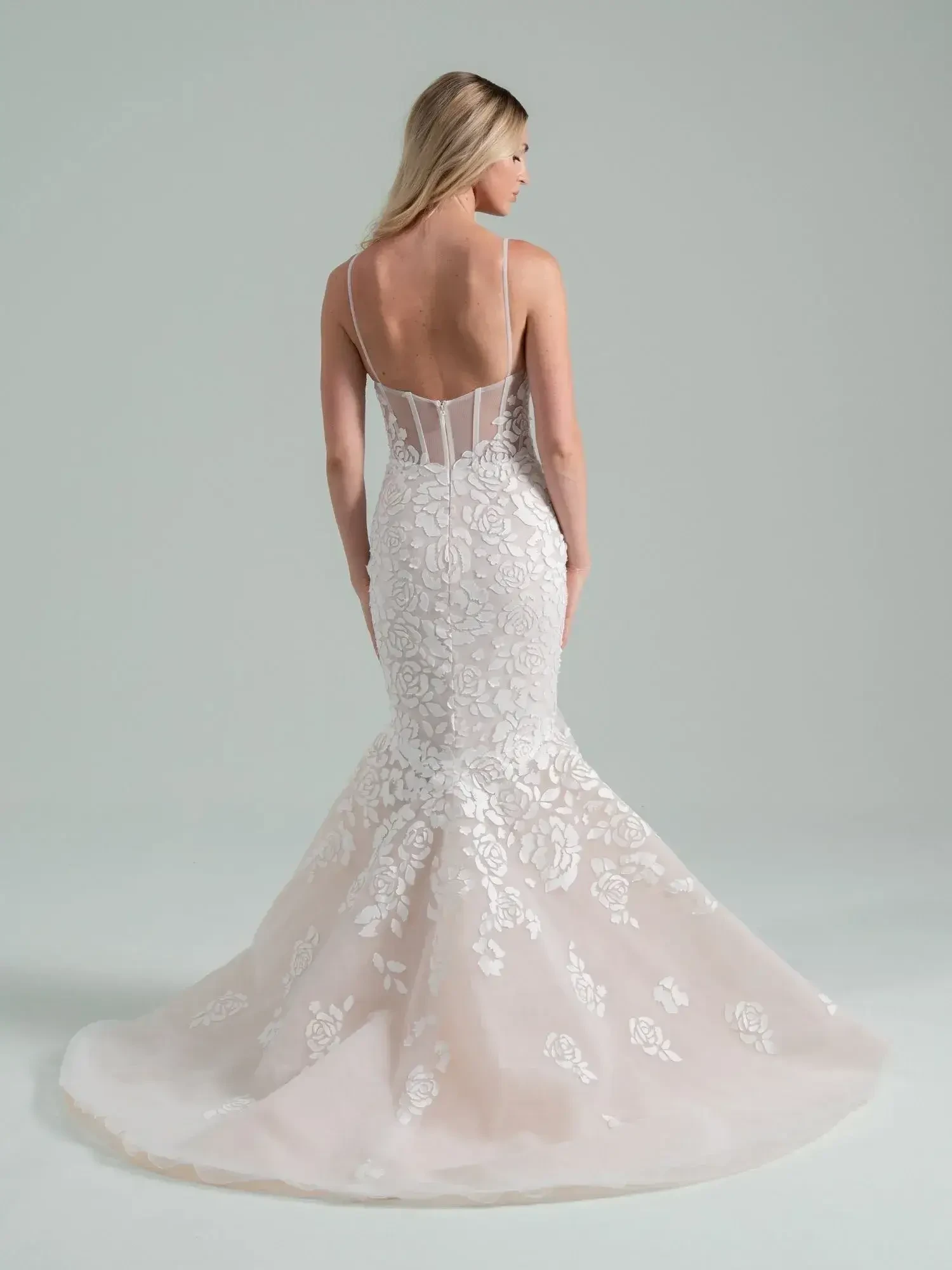 A woman wearing a fitted mermaid wedding dress with intricate floral lace detailing, showing the back of the dress.