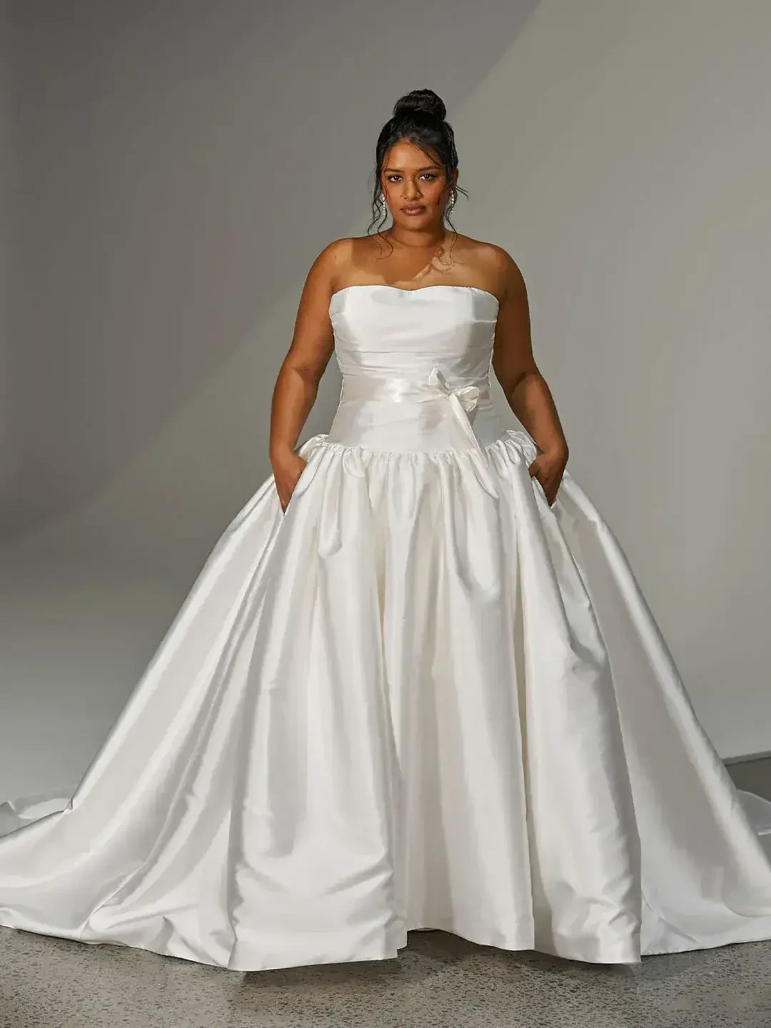 A person wearing a strapless white gown with pockets, standing against a light background.