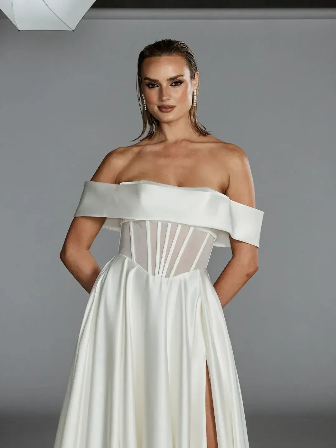 A woman wearing an elegant off-the-shoulder white gown with a fitted bodice and a flowing skirt.
