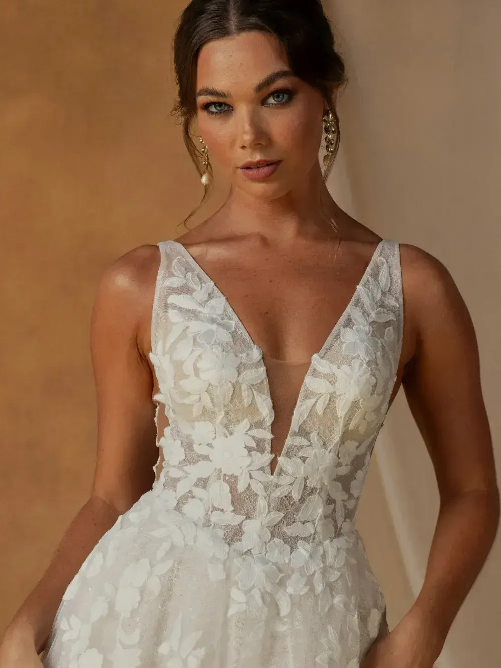 A person wearing a floral lace gown with a deep V-neckline, standing in front of a neutral background.